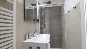 A modern bathroom with a glass-enclosed shower, a white vanity, and a mirror above the sink. - Bligny 39 B (Milan)