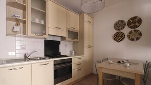 A kitchen with beige cabinets, a black stove, and a dining area with a wooden table and chairs. - Bligny 39 B (Milan)