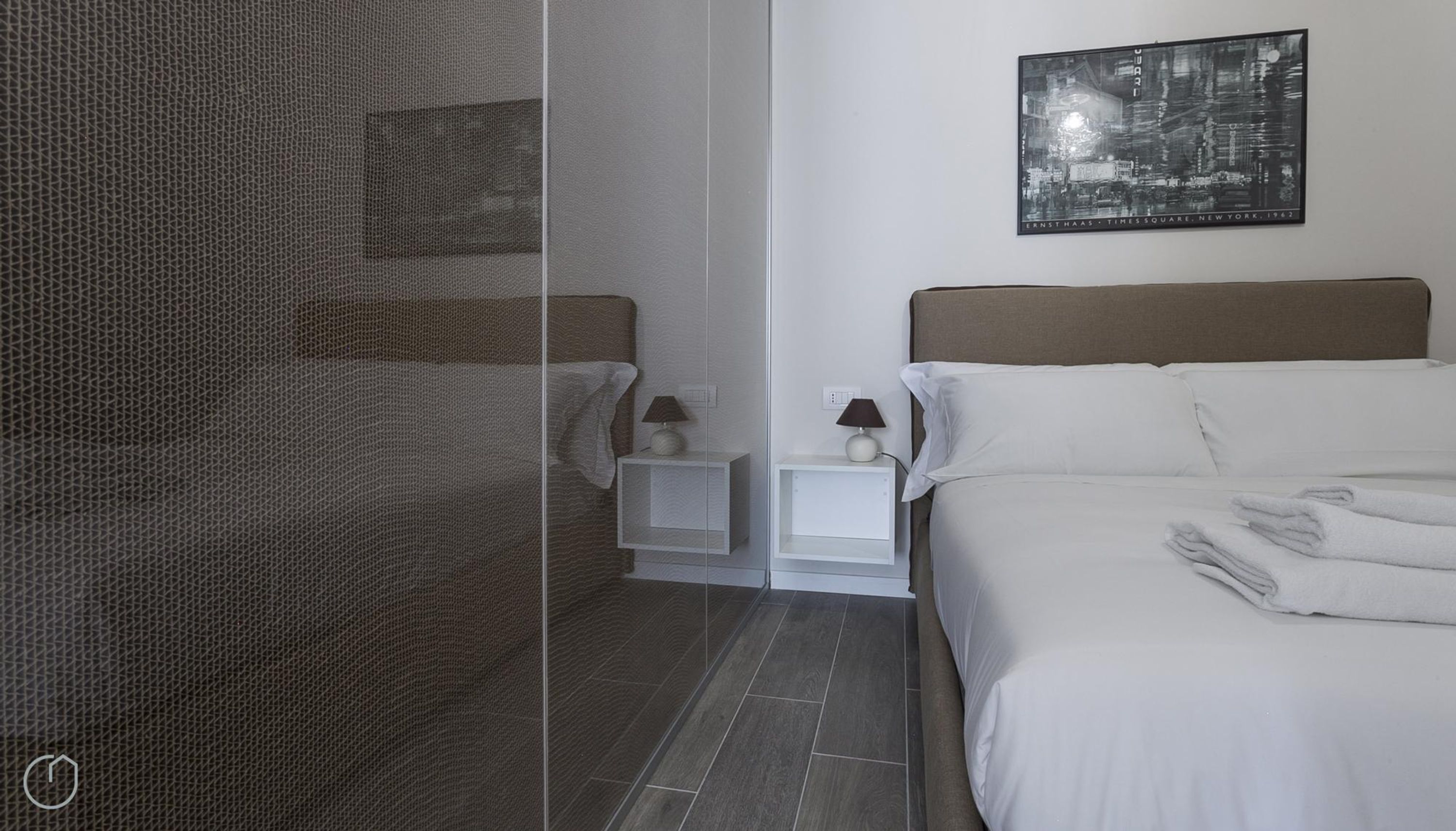 A modern hotel room with a bed, a nightstand, a lamp, and a framed picture on the wall.