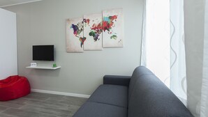 A living room with a grey sofa, a red bean bag, a flat-screen TV on a white shelf, and two abstract world maps on the wall. - Italianway Easy - Cadorna 10 Mono B (Milan)