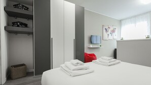 A modern hotel room with a bed, a red chair, a TV, and a wardrobe with shelves. - Italianway Easy - Cadorna 10 Mono B (Milan)