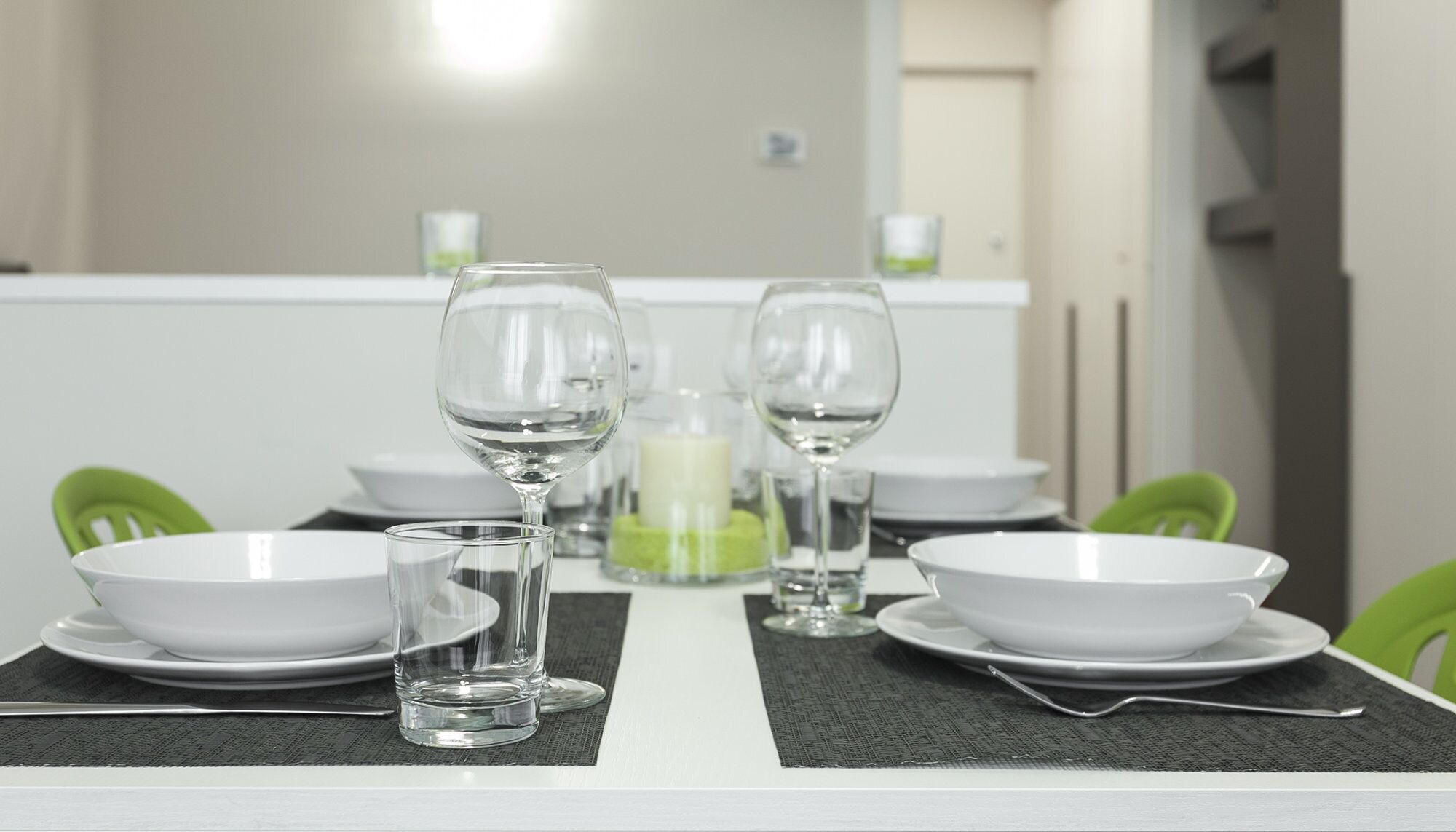 A dining table set with white bowls, wine glasses, and a candle.