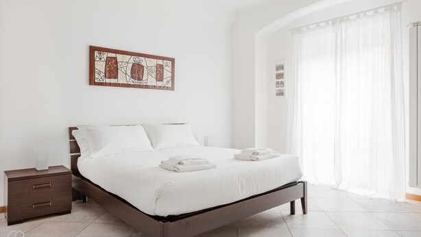 A modern bedroom with a large bed, a nightstand, and a wall-mounted artwork. - Italianway Easy - Cerano 15 (Milan)