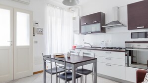 A modern kitchen with white cabinets, a gas stove, and a microwave. There is a dining table with chairs and a window with curtains. - Italianway Easy - Cerano 15 (Milan)