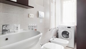 A modern bathroom with a large bathtub, a toilet, and a washing machine. - Italianway Easy - Cerano 15 (Milan)