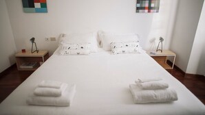 Un lit bien fait, avec du linge de lit blanc et deux oreillers, flanqué de deux tables de chevet sur lesquelles reposent des lampes et des livres.