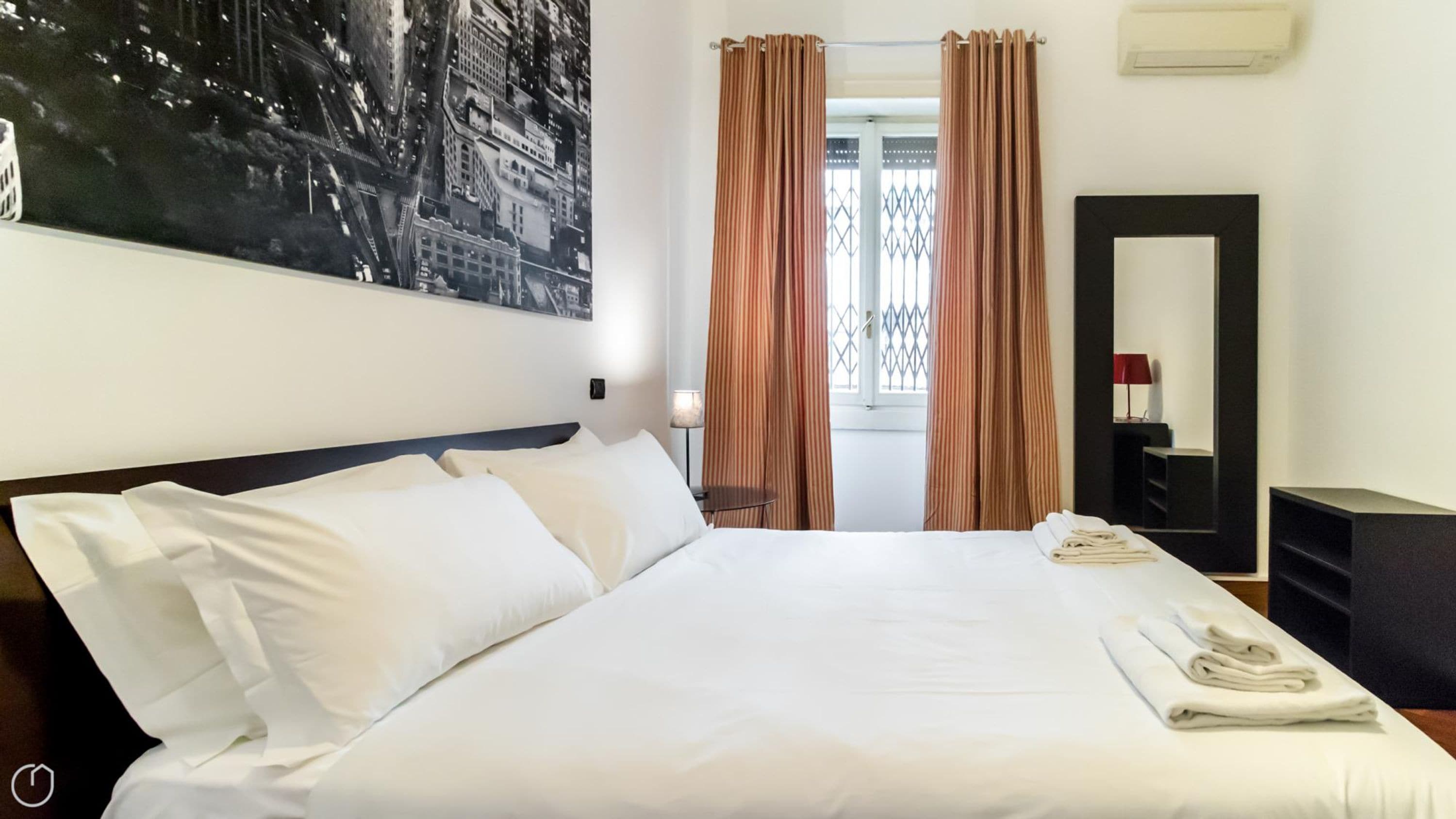 A hotel room with a large bed, a nightstand, a mirror, and a window with curtains.