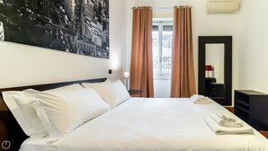 A hotel room with a large bed, a nightstand, a mirror, and a window with curtains. - Italianway Easy - Cristoforo Colombo 1 (Milan)