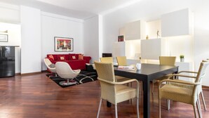 A modern living room with a red sofa, white armchair, and wicker chairs around a black dining table. - Italianway Easy - Cristoforo Colombo 1 (Milan)