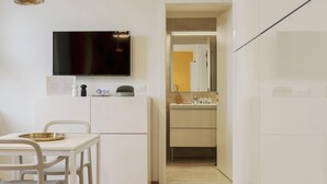 A compact room with a dining table, a flat-screen TV mounted on the wall, a small cabinet, and a mirror above the sink. - Mono A (Milan)