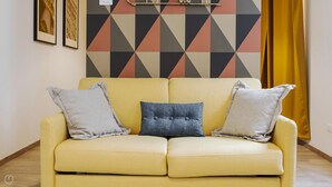 A yellow sofa with three pillows, a geometric patterned wall, and a yellow curtain. - Mono A (Milan)