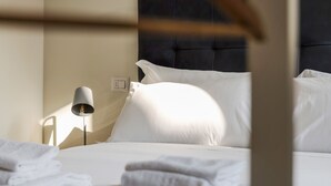A neatly made bed with white linens, a bedside lamp, and a power outlet on the wall. - Mono A (Milan)