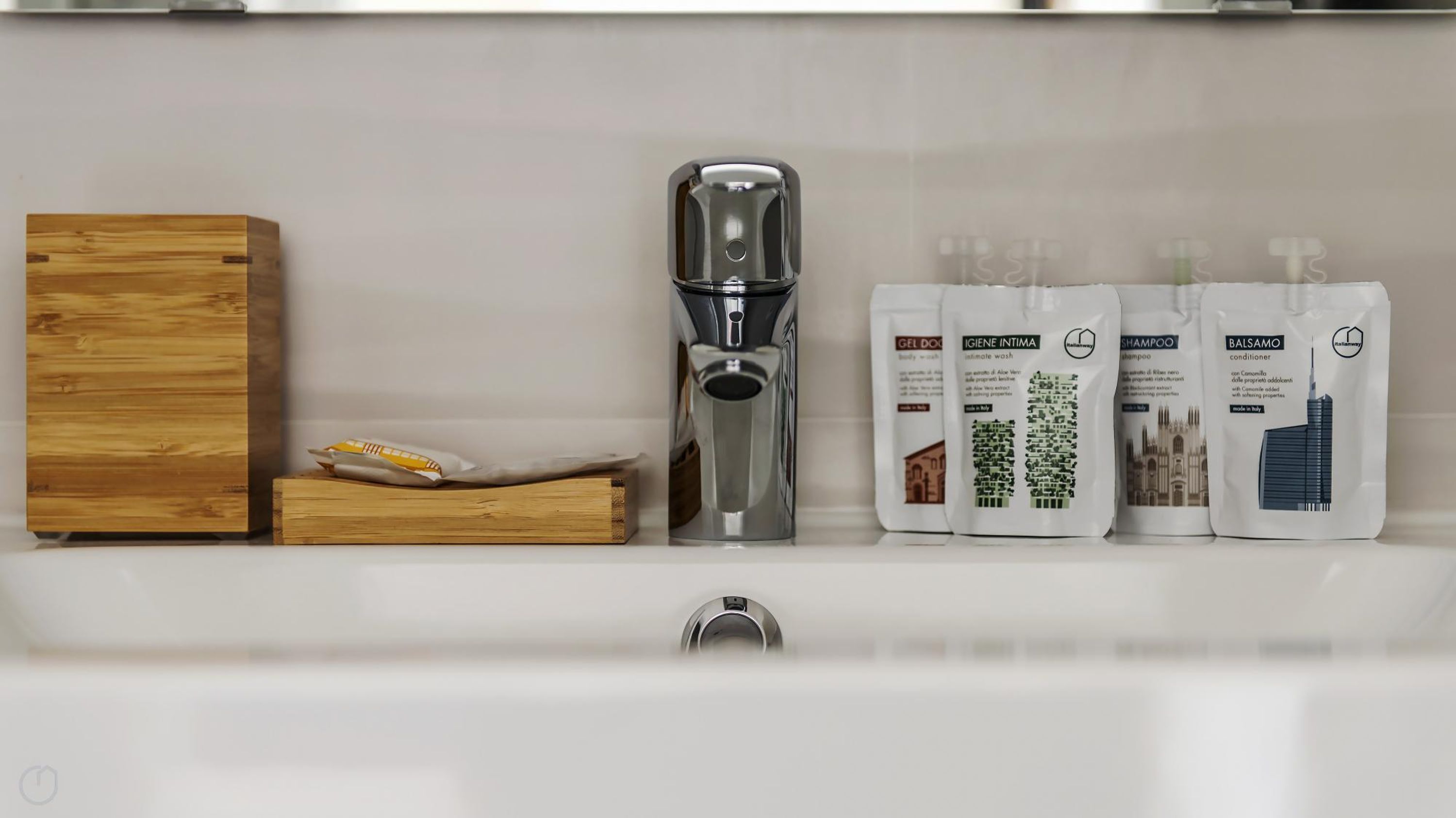 A bathroom with a modern faucet, a wooden box, and three toiletry bags.