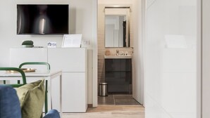 A compact kitchen with a flat-screen TV, a small refrigerator, and a dining area with a chair and table. - Mono A (Milan)