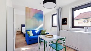 A modern room with a blue sofa, a white table, green chairs, a large abstract painting, a window with curtains, and a welcome sign. - Mono A (Milan)