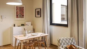 A dining area with a wooden table, clear chairs, a white cabinet, and a window with curtains. - Mono B (Milan)