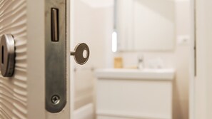 Un baño con un lavamanos blanco, un espejo y una puerta con un ojo de cerradura.
