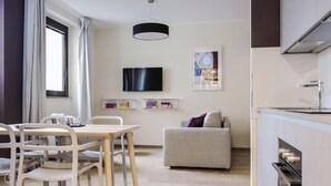 Una habitación moderna con una mesa de comedor, sillas, un sofá, un televisor y una zona de cocina.