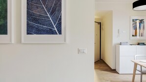 Un pasillo con obras de arte enmarcadas, un armario blanco y un escritorio.