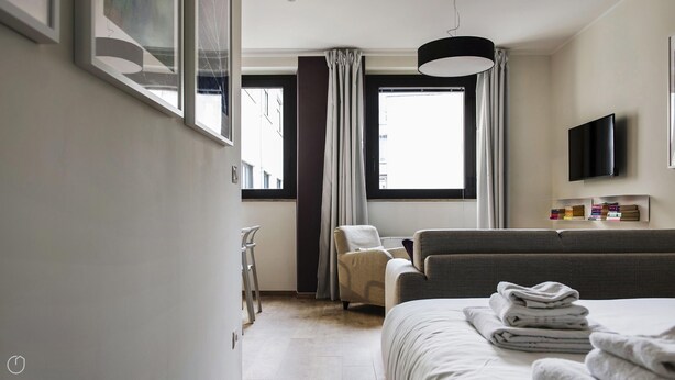 Una habitación de hotel moderna con una cama, un sofá, un televisor y una ventana con cortinas.