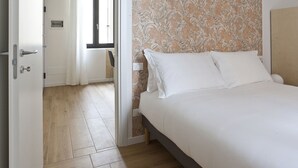 A bedroom with a bed, white bedding, a wooden floor, and a patterned wallpaper. - Italianway Easy - Caretto 4 - Tebaldi (Milan)