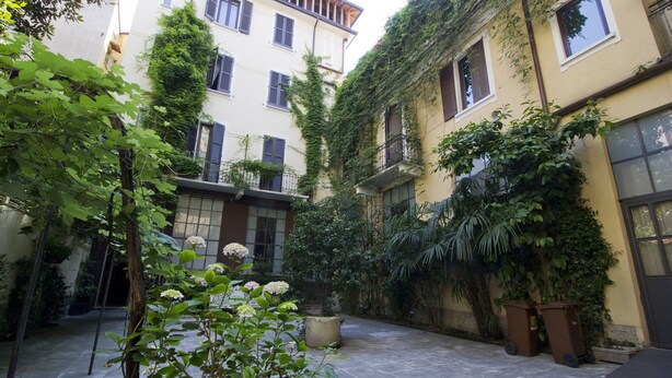 A courtyard with a tiled floor, surrounded by buildings with multiple windows and balconies. - Italianway Easy - Caretto 4 - Tebaldi (Milan)