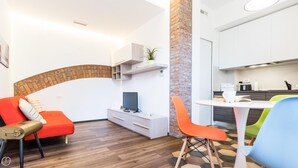 A modern living room with a curved brick wall, a TV on a white cabinet, and a dining area with colorful chairs. - Italianway Easy - Ciaia 6 B (Milan)