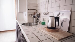 Eine Küche mit Spüle aus Edelstahl, Wasserkocher und Schneidebrett auf der Arbeitsfläche.