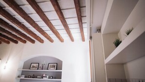 Ein Zimmer mit freiliegenden Holzbalken, einer weißen Wand und einem Regal mit gerahmten Fotos und Dekorationen.