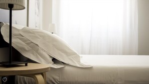 Una habitación de hotel con una cama bien hecha, una mesita de noche y una lámpara.