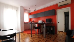 A compact kitchen with a dining area, featuring a modern design with red walls and wooden flooring. - Italianway Easy - Corso Lodi 78 (Milan)