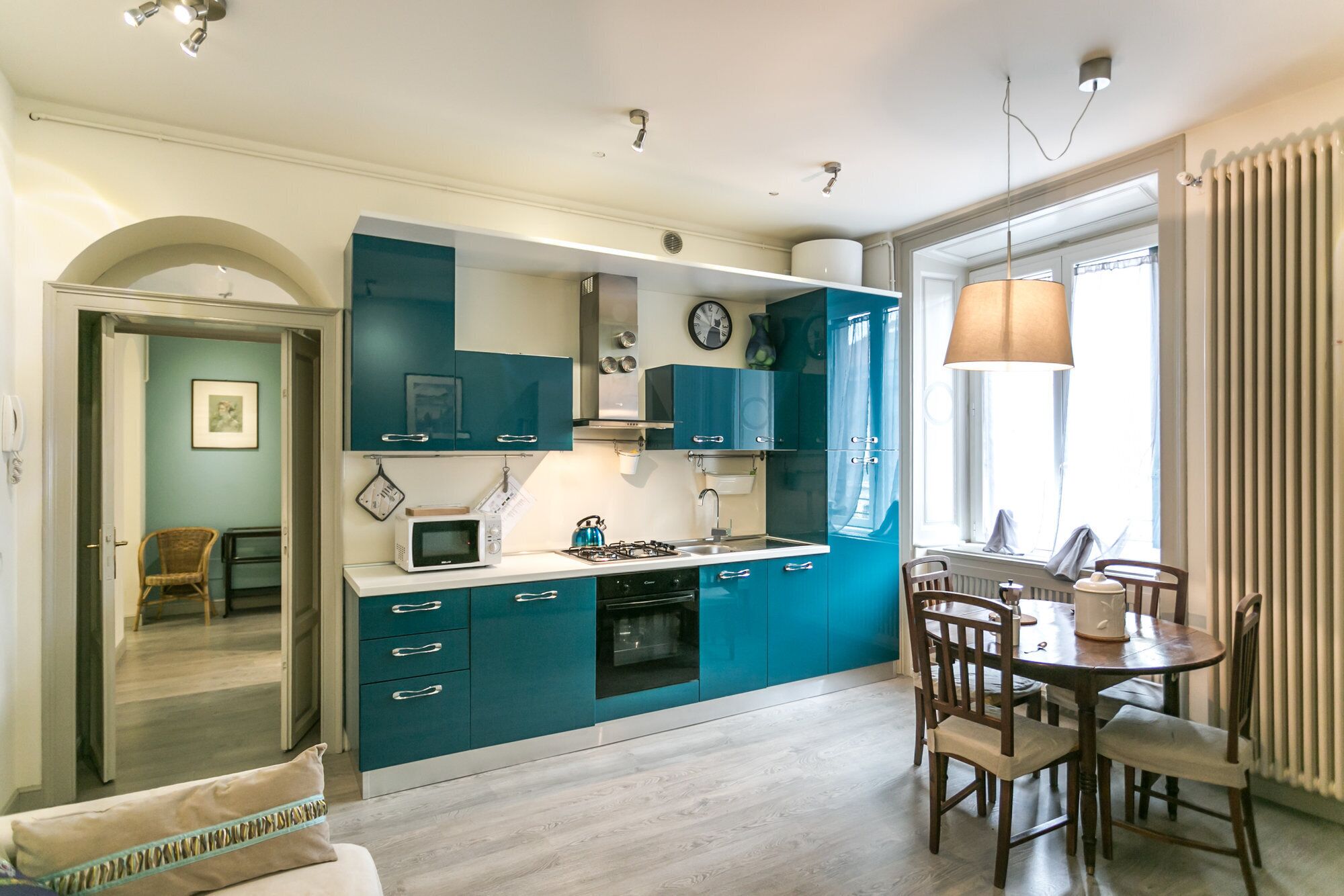 Une cuisine moderne avec des armoires de couleur turquoise, un four à micro-ondes, une cuisinière et un coin repas comprenant des chaises et une table en bois.