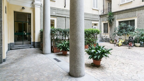 A courtyard with stone flooring, columns, potted plants, and bicycles. - Mi-clod9a3 - Corso Lodi 9 (Milan)
