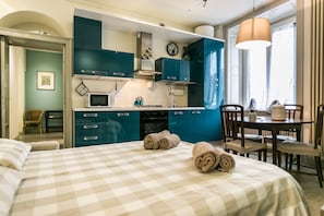 Une chambre à coucher de taille modeste, avec une couvre-lit à carreaux, une petite cuisine équipée avec des meubles de couleur turquoise et un coin repas comprenant une table et des chaises.