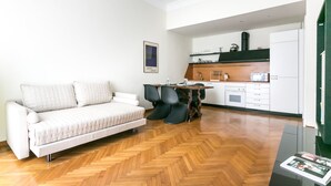 A modern living room with a sofa, a dining table, and a kitchen area with a microwave and oven. - Italianway Easy - Da Procida 25 (Milan)