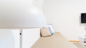 Un lit bien fait, avec une tête de lit blanche, une table de chevet sur laquelle se trouve un téléviseur à écran plat, et une lampe fixée au mur.