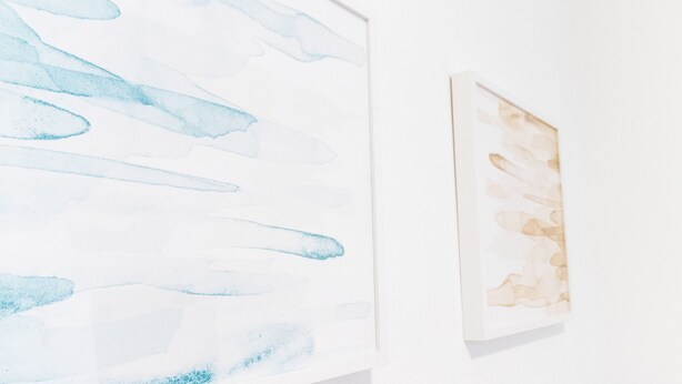 Een muur met twee kunstwerken; één abstract met blauwe vormen, de ander in bruine tinten.