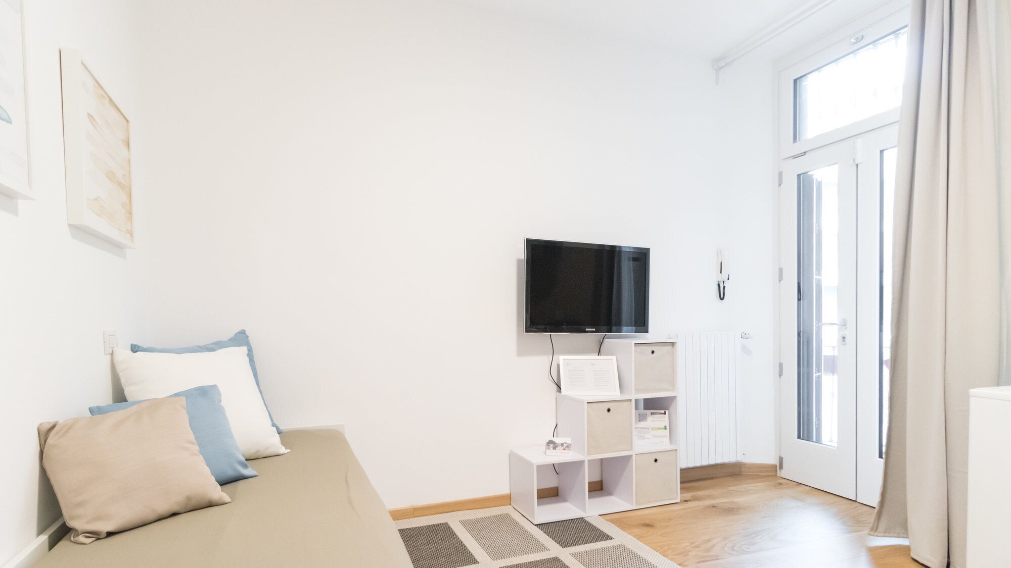 Un salon minimaliste avec un canapé, un téléviseur à écran plat et un meuble de rangement blanc.