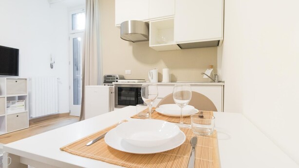 Eine moderne Küche mit weißen Schränken, einer Mikrowelle, einem Toaster und einem Wasserkocher. Ein Esstisch ist gedeckt mit Tellern, Gläsern und Besteck.