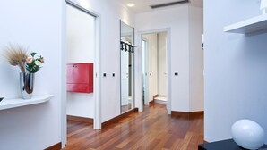 A hallway with wooden flooring, a red utility cabinet, a white door, and a white spherical object on a black surface. - Italianway Easy - Dogana 3 (Milan)