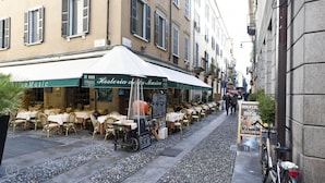 An outdoor café with tables and chairs, a sign for 'Hosteria della Musica', and a bicycle parked on the sidewalk. - Italianway Easy - Fiori Chiari 20 (Milan)