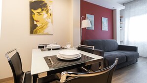 En spiseplads med et bord dækket til to, en grå sofa og en rød væg.
