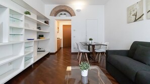 A modern living room with a sofa, a dining table with chairs, and a kitchen area with a brick archway.
