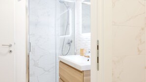 Ein modernes Badezimmer mit Duschkabine aus Glas, einem weißen Waschbecken und Holzschränken.