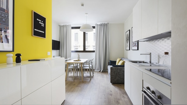 Een moderne keuken met witte kastjes, een eethoek met een tafel en stoelen, en een bank.