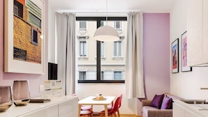 Un salon moderne avec un coin repas, de grandes fenêtres avec des rideaux, un luminaire suspendu et des œuvres d’art accrochées aux murs.