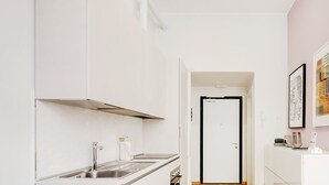 Une cuisine moderne avec des meubles blancs, un évier en acier inoxydable et une porte à cadre noir donnant sur une autre pièce.