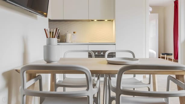 A modern dining area with a wooden table and white chairs, a white vase with utensils, and a kitchen in the background. - Mi-brgz1c2 Bergonzoli Place - Bilo B - Blues (Milan)