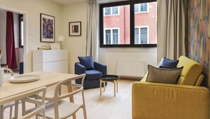 A living room with a sofa, a chair, a small table, and a window with a view of buildings.