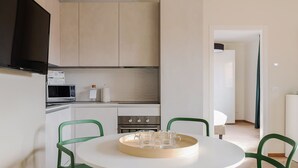 A modern kitchen with white cabinets, a microwave, and a stove. There is a dining table with two chairs and a tray with glasses. - Mi-brgz1c4 Bergonzoli Place - Bilo B - Canoe (Milan)